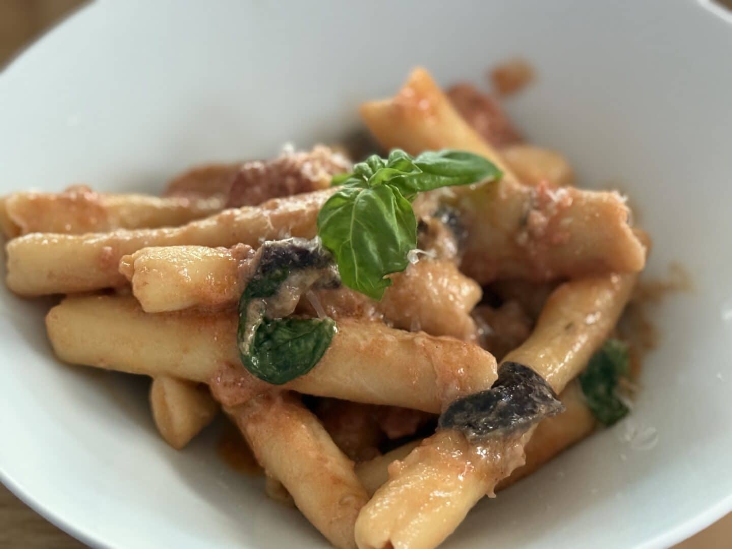 Eine weiße Schale mit Nudeln in einer cremigen Tomatensauce, garniert mit frischen Basilikumblättern und Auberginenstücken.